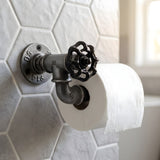 Dérouleur papier WC à volant noir en fonte fixé sur un mur carrelé, avec un rouleau de papier toilette