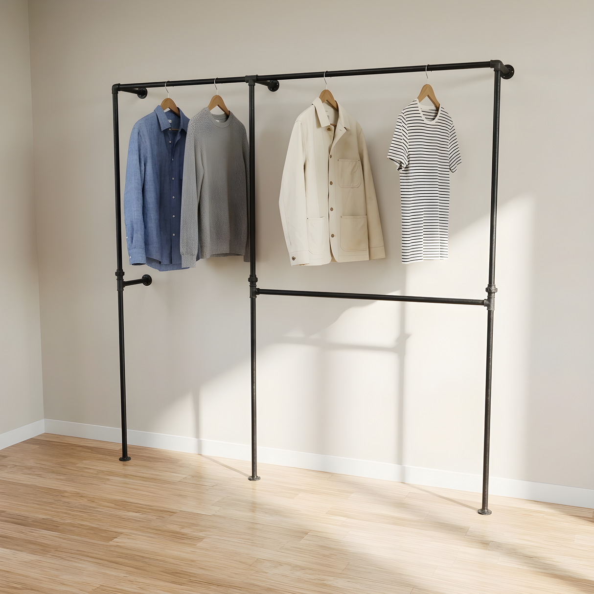 Penderie ouverte deux baies en tuyaux de plomberie noirs Ø 27 mm fixée au mur, chemises et vestes sur cintres en bois, parquet clair et lumière naturelle